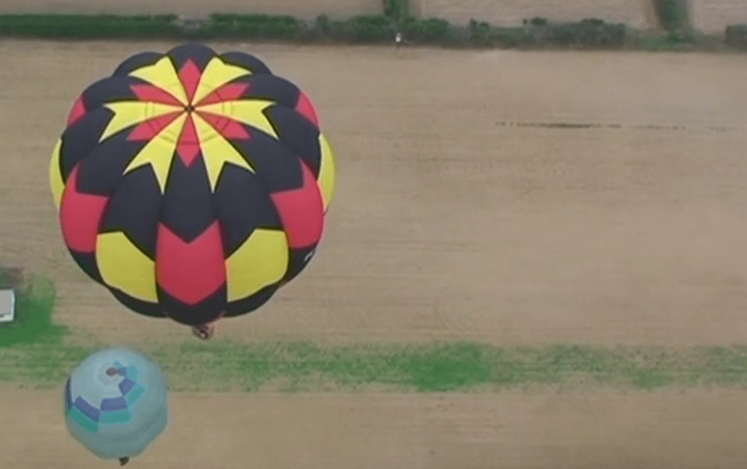 Hot air balloons rise over bare fields